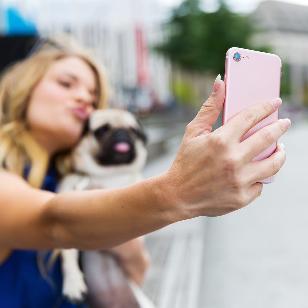 image showing woman holding a pug, taking a selfie