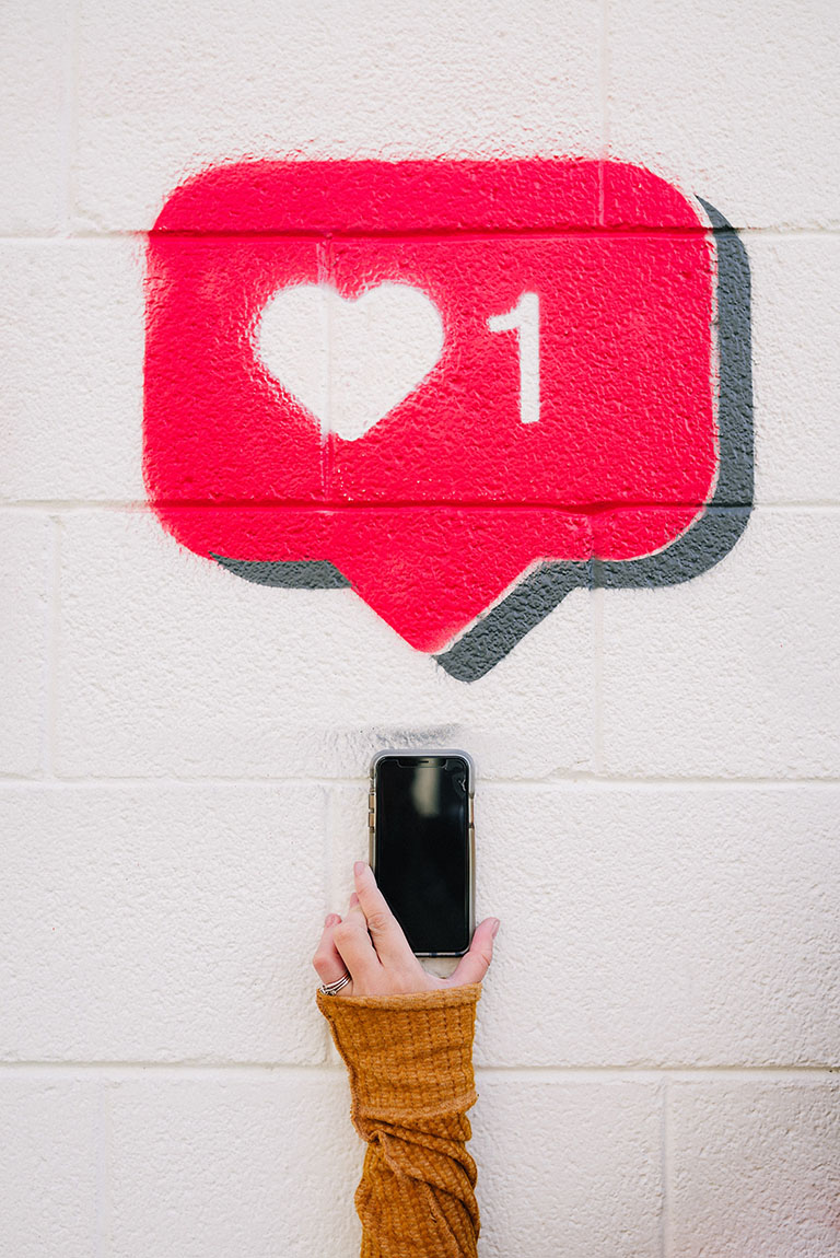 image showing a hand touching graffiti art depict a mobile phone with a big like heart above it