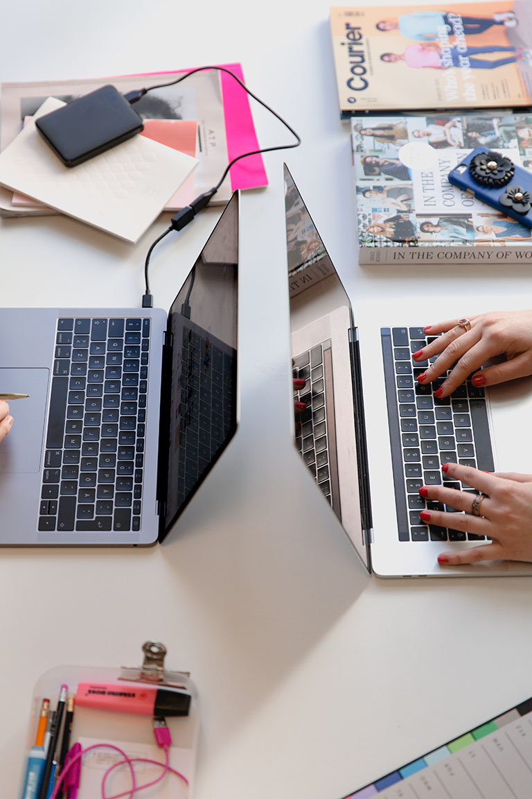 image showing to laptops opposite each other on a desk with people typing on them